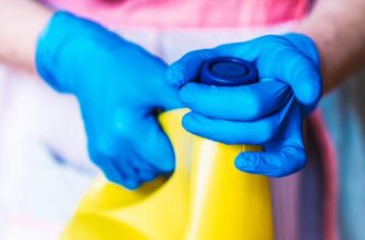 Someone wearing gloves removing the lid from a bottle of bleach