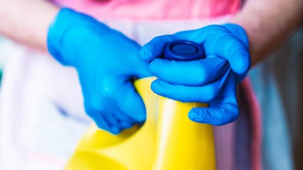 Someone wearing gloves removing the lid from a bottle of bleach Someone wearing gloves removing the lid from a bottle of bleach
