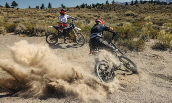 A rider sitting on a Zero XE watching another rider doing donuts in the dirt on a Zero XB. A rider sitting on a Zero XE watching another rider doing donuts in the dirt on a Zero XB.