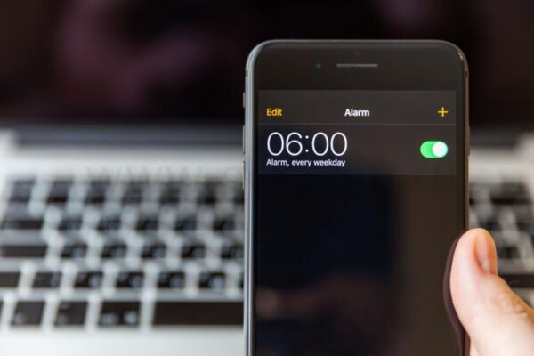Список будильников на экране iPhone перед MacBook.