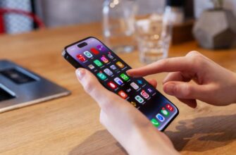 Человек, использующий iPhone за столом, позади которого находится стакан.