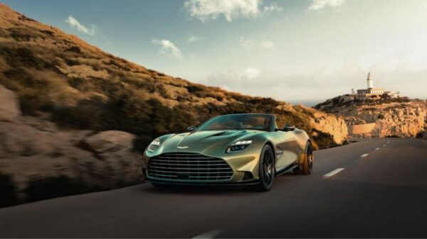 Передний вид нового Aston Martin Vanquish Volante, движущегося по побережью на фоне маяка.