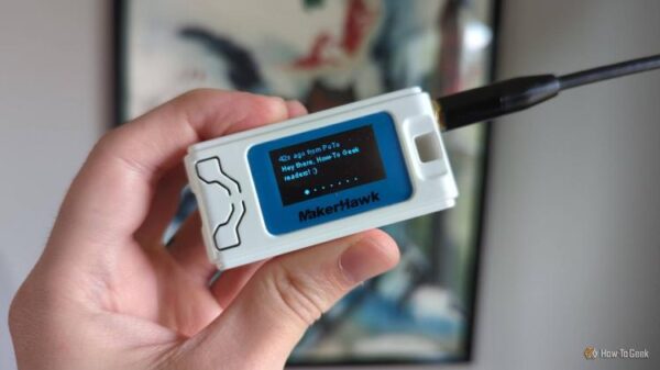A hand holding a Heltec V3 LoRa radio in a MakerHawk case, with a message on the radio's OLED display reading