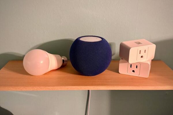 Синий HomePod mini рядом с двумя умными розетками и умной лампочкой на полке.