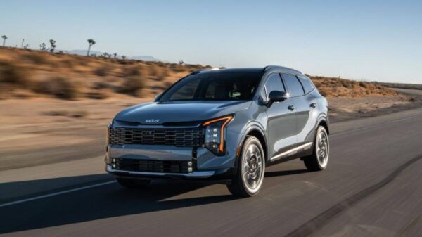 Dynamic front 3/4 shot of a 2026 Kia Sportage HEV driving on a country road.