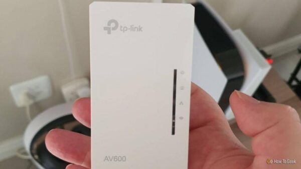 Рука держит сетевой адаптер TP-Link AV600 Powerline перед PS5.