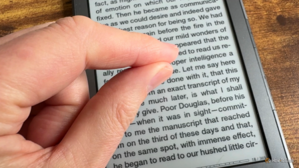 Two fingers making a pinch gesture held over a Kindle 4 with a book open on the screen.